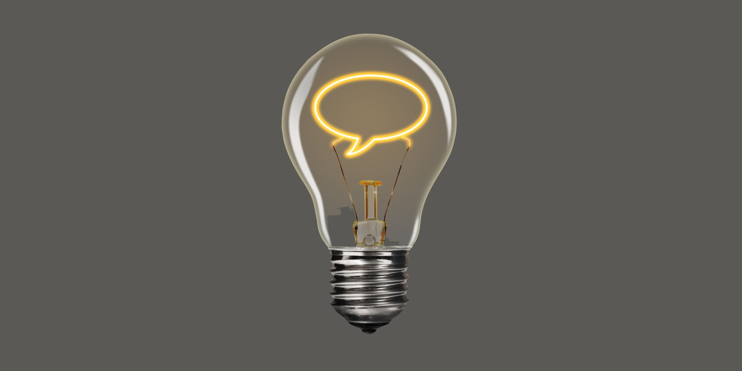 A photo of a lightbulb on the grey background. Instead of the regular lightbulb filament, the filament is in the shape of a speech bubble. It is glowing yellow.